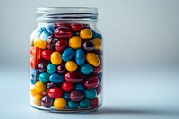 Glass jar filled with colorful round candies in red, blue, yellow, orange and brown colors on white background for sweet treats and confectionery designs.
