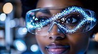 Young African American female scientist wearing protective eyewear with glowing digital particles effect, representing innovation in science and technology research.