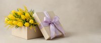 Kraft gift box with purple ribbon bow and yellow tulips with mimosa flowers on beige background, spring holiday celebration concept.