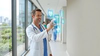 Middle-aged Caucasian male doctor in white coat using futuristic holographic medical interface technology in modern hospital corridor for healthcare innovation.