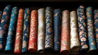 Row of vintage decorative paper rolls featuring floral and ornamental patterns in blue, coral, and cream colors arranged on dark background.