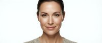 Professional businesswoman with natural makeup and confident smile wearing beige sweater against white background for corporate headshot photography.