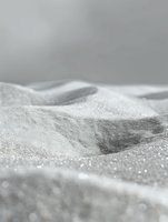 Macro view of white crystalline powder forming abstract dunes and hills with soft shadows and sparkles, creating minimalist monochrome landscape.
