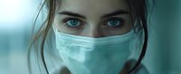 Young woman with intense blue eyes wearing protective medical face mask against turquoise background, portraying healthcare and pandemic awareness.