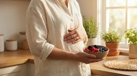 Pregnant woman holding a bowl of fresh berries in a bright kitchen, embracing healthy nutrition during pregnancy for mother and baby wellness.