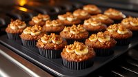 Chocolate banana cupcakes topped with caramel buttercream frosting and crushed walnuts on black baking tray. Homemade dessert with rich decorative swirls and golden nuts.