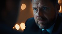 Middle-aged Caucasian businessman with beard and piercing blue eyes in dark suit against blurred bokeh lights background, dramatic cinematic portrait lighting.