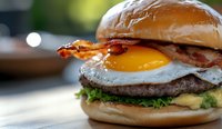 Juicy beef burger topped with crispy bacon, sunny side up egg, fresh lettuce, and melted cheese on toasted bun, extreme close up with selective focus.