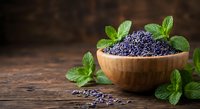 Dried lavender flowers in wooden bowl with fresh mint leaves on rustic table. Natural herbs for aromatherapy, cooking, crafts and wellness products.