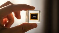 Hand holding transparent glass cube with golden gift label in warm sunlight for luxury branding and premium product presentation concepts.