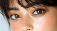 Close up portrait of young Asian woman with natural makeup, brown eyes and black hair against light background, showing flawless glowing skin and long eyelashes.