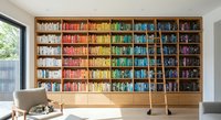 Modern home library with floor-to-ceiling wooden bookshelf displaying colorful books organized by rainbow spectrum in bright contemporary living room.