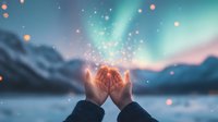 Magical glowing light particles rising from cupped hands against winter mountain landscape with aurora borealis and snowy peaks in dreamy twilight atmosphere.