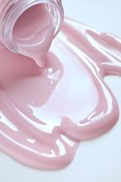 Luxurious pink cosmetic cream pouring from jar creating smooth glossy texture on white surface, macro shot showing skincare product consistency and flow.
