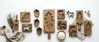 Wooden molds and carved kitchen tools arranged flat lay with dried herbs and linen cloth on white background for baking and cooking.