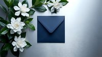 Navy blue envelope surrounded by white gardenia flowers and green leaves on light background for wedding invitations and elegant correspondence.