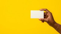 Hand of a male with dark skin tone holding a blank white business card against a bright yellow background, suitable for branding, marketing, and corporate identity presentations.