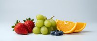 Fresh mixed fruits including strawberries, green grapes, orange slices and blueberries arranged on white background for healthy eating concepts.