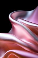 Smooth flowing pink satin fabric with elegant folds and curves creates luxurious waves against dark background, highlighting soft metallic sheen and gentle shadows.