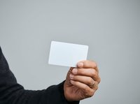 Close-up of a hand holding a blank white card against a neutral gray background, suitable for business, marketing, and branding mockups.