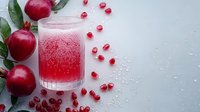 Fresh pomegranate juice in glass with scattered seeds and whole fruits on light background, fizzy red drink with bubbles and ice for healthy beverage concept.