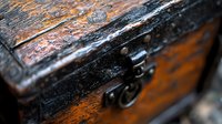 Antique wooden treasure chest with rustic metal latch and weathered patina showing rich wood grain texture and vintage details in dramatic macro photography.