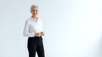 Confident mature businesswoman with short gray hair in white shirt and black pants standing against white background for corporate presentations.