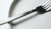 Stainless steel fork resting on a speckled ceramic plate, minimalist dining concept with soft natural light and neutral tones.