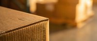 Stack of brown corrugated cardboard shipping boxes in warehouse storage facility with warm lighting for logistics and delivery services.