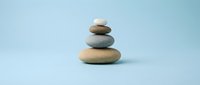 Balanced stack of smooth river stones in earth tones on soft blue background for meditation wellness spa and mindfulness concepts.