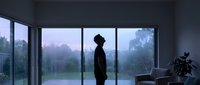 Young man silhouette standing by large windows in modern minimalist room during twilight with misty forest view creating contemplative mood for wellness concepts.