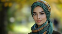 Young Middle Eastern woman wearing emerald green hijab and traditional headscarf smiling confidently against soft bokeh background in natural outdoor setting.