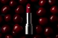 Red lipstick with heart detail on dark background surrounded by glossy cherry-like spheres creating luxurious cosmetic composition with romantic mood.