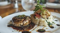 Grilled beef tenderloin steak with red wine reduction sauce, served with creamy mashed potatoes and fresh microgreens garnish on white plate, fine dining presentation.