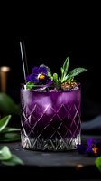 Purple cocktail garnished with fresh viola flowers and herbs in crystal glass on dark background. Refreshing summer drink with edible flowers and ice.