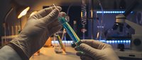 Scientist in protective gloves holding test tube with green liquid in modern laboratory with advanced equipment and blue LED lighting for research.
