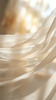 Flowing cream-colored fabric with soft waves and gentle folds, creating an elegant, luxurious texture. Warm, diffused light enhances the delicate draping for design and lifestyle projects.