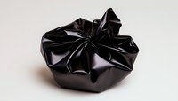 Crumpled black glossy fabric or leather material forming abstract sculptural shape against neutral background, showcasing texture and light reflection. Suitable for luxury design.