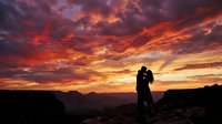 Silhouette of couple embracing on mountain peak at dramatic sunset with vibrant orange and red sky, romantic outdoor engagement or wedding moment for travel and lifestyle content.