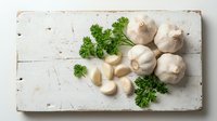 Fresh garlic bulbs and cloves with green parsley herbs arranged on rustic white wooden cutting board for cooking and culinary preparation.