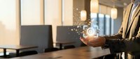 Businessman holding glowing light bulb with digital sparkles in modern office workspace, representing innovation, creativity, and business solutions for corporate success.