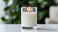 White scented candle with triple flame burning in clear glass container against blurred green background, creating cozy atmosphere for spa and relaxation.