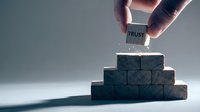 Hand placing wooden block with trust text on pyramid of dark cubes representing business foundation and reliability concepts for corporate presentations.