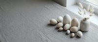 Natural wooden eggs in various sizes scattered on rustic gray wood surface near window with soft natural lighting for Easter decoration and craft projects.