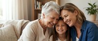 Happy three generation family embracing on couch at home. Grandmother, mother and daughter sharing loving moment together in cozy living room interior.