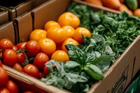 Fresh organic tomatoes and leafy greens in wooden crate at farmers market, selective focus on vibrant produce showcasing local harvest and healthy eating.