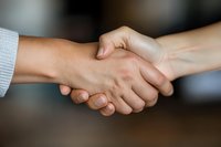 Close-up of firm business handshake between two people wearing light colored clothing, symbolizing trust, agreement and professional partnership on blurred background.