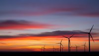 Wind turbines silhouetted against dramatic sunset sky with orange and purple clouds. Renewable energy farm at dusk for sustainable power generation concepts.