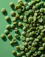 Fresh dried green peas scattered on green background with natural shadows, top view. Perfect for healthy eating, vegetarian cuisine, and food industry designs.