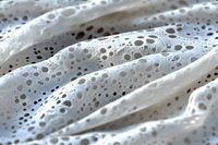 Macro view of white porous fabric texture with tiny holes and water droplets creating abstract pattern. Natural light highlights delicate surface details.